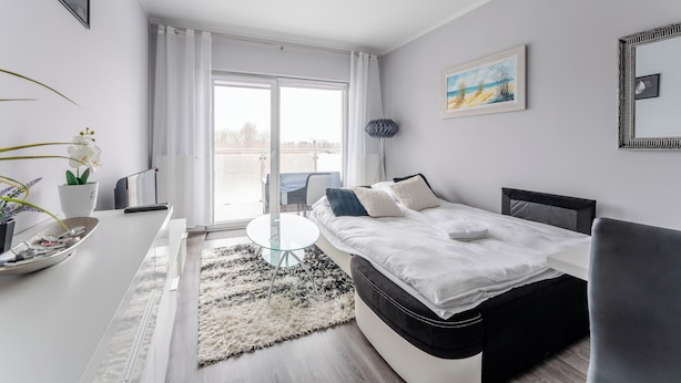 Ein modernes Schlafzimmer mit einem Bett, einem kleinen Tisch, einem Stuhl und Blick ins Freie durch ein großes Fenster.