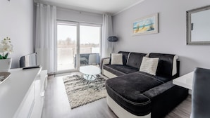 Ein modernes Wohnzimmer mit einem schwarzen Sofa, einem weißen Couchtisch und einem großen Fenster mit Vorhängen.