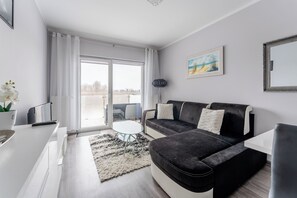 A modern living room with a black sofa, a white coffee table, and a large window with curtains. - Wielkopolska Cozy Apartment (Kołobrzeg)