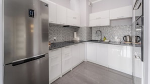 Eine moderne Küche mit weißen Schränken, einem Edelstahl-Kühlschrank, einer gefliesten Spritzschutzwand und einer schwarzen Arbeitsplatte.