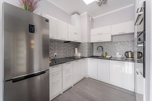 A modern kitchen with white cabinets, a stainless steel refrigerator, a tiled backsplash, and a black countertop. - Wielkopolska Cozy Apartment (Kołobrzeg)