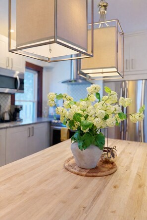 Cocina de diseño moderno, con encimera de madera, un florero con flores blancas e iluminación colgante.
