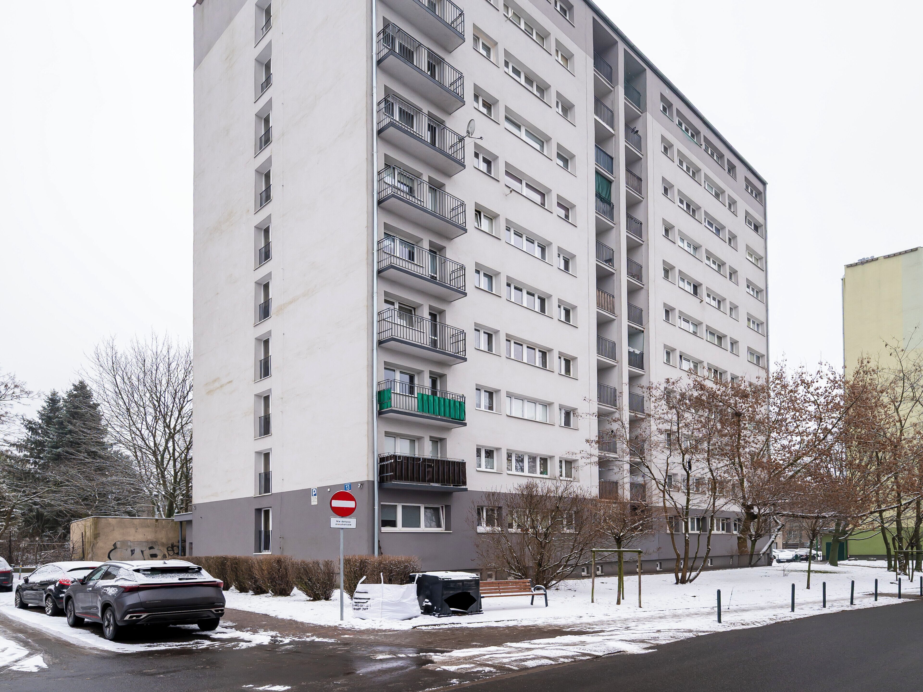 Un edificio residencial de varios pisos con balcones, una señal de 'prohibido el paso' y coches aparcados.