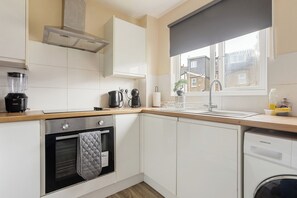 Eine moderne Küche mit weißen Schränken, einem Backofen, einem Geschirrspüler und einem Fenster mit Blick auf eine Wohngegend.