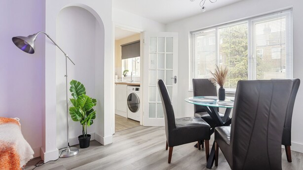 A modern living room with a dining area, a floor lamp, a potted plant, and a view of the kitchen through an open door. - Modern 2BR Flat, 20 mins train to Central London, 7mins to Selhurst Park Stadium (London)