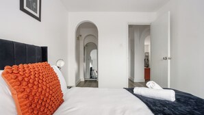 A hotel room with a bed, a large orange textured pillow, a white pillow, a dark blue blanket, and a white towel on the bed. - Modern 2BR Flat, 20 mins train to Central London, 7mins to Selhurst Park Stadium (London)