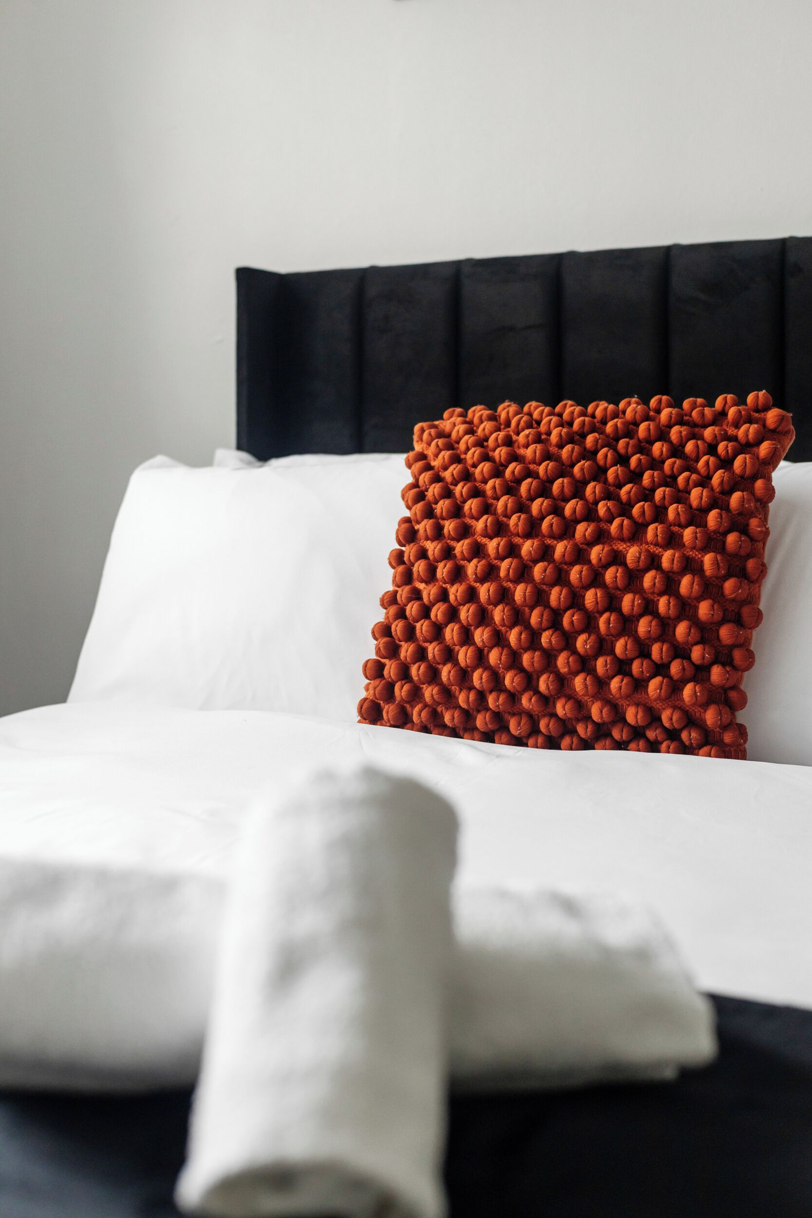 Een keurig opgemaakt bed met witte lakens en een enkel kussen met oranje textuur.