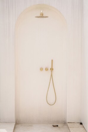 A white shower enclosure with a gold showerhead and controls. - House Of Lucky Seseh (Cemagi)