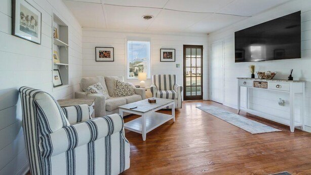A spacious living room with a large TV, a sofa, a striped armchair, and a coffee table. - 37372 7th St.- A perfect beach retreat- nightly pet friendly rental. (Rehoboth Beach)