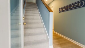 A staircase with a carpeted finish, a wooden handrail, and a wall sign reading 'BEACH HOUSE'.