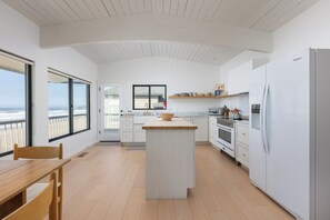 Eine moderne Küche mit Kochinsel, weißen Schränken und Blick auf den Strand durch große Fenster.