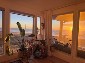 A room with large windows, a variety of potted plants, and a view of the sunset over the ocean. - Pacific Perch-Lux, 4 bed, oceanfront with huge views. (Pacific City)