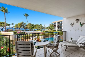 Ein Balkon mit Tisch für zwei Personen, mit Blick auf einen Pool und einen Resort-Bereich mit Palmen und Gebäuden.