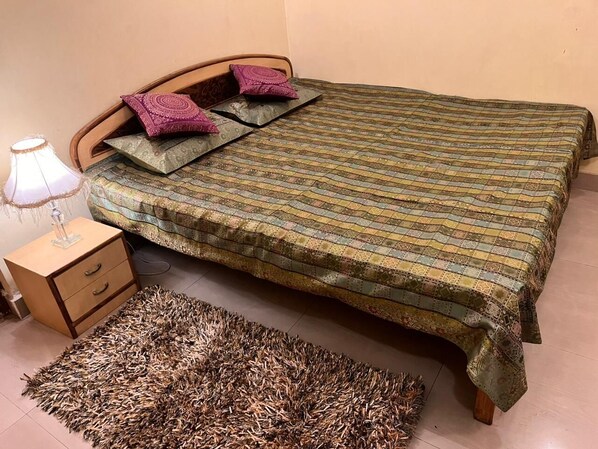 A bedroom with a bed, a nightstand, a lamp, and a rug. - SHEETAL HOMESTAY (Varanasi)
