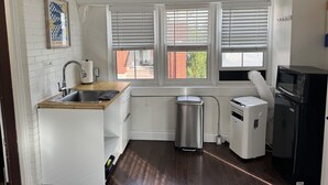 A compact kitchen with white cabinetry, a wooden countertop, a stainless steel sink, a compact refrigerator, and a small trash bin. - Private Downtown Kitchener Studio | Parking, Kitchenette, Wi-Fi (Kitchener)