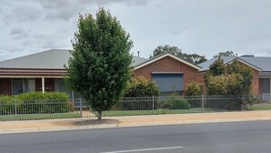 Uma rua residencial com duas casas de tijolo, uma delas com garagem e uma árvore na frente.