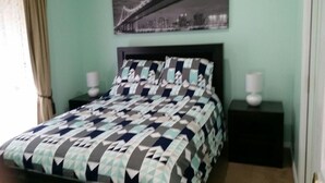 Uma cama com colcha estampada, duas mesas de cabeceira com abajures e um quadro com vista para a cidade na parede.