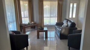 Sala de estar com sofá, duas poltronas, mesa de centro e mesa lateral. Cortinas nas janelas e uma planta na mesa lateral.
