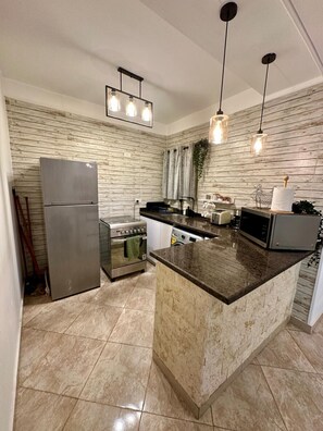A modern kitchen with a central island, stainless steel appliances, and wooden panel walls. - Elegant 2BR Heliopolis Suite | Private Garden Terrace & A/C (Heliopolis)