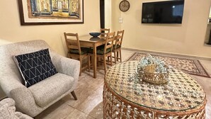 A living room with a sofa, a round coffee table, a dining area with chairs, a wall-mounted TV, and a framed picture. - The Helio Suite Modern 1 bdrm (Heliopolis)
