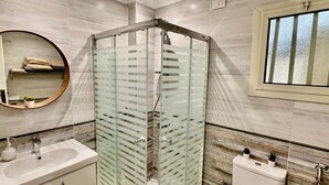 A modern bathroom with a glass-enclosed shower, a toilet, and a sink with a mirror above it. - The Helio Suite Modern 1 bdrm (Heliopolis)