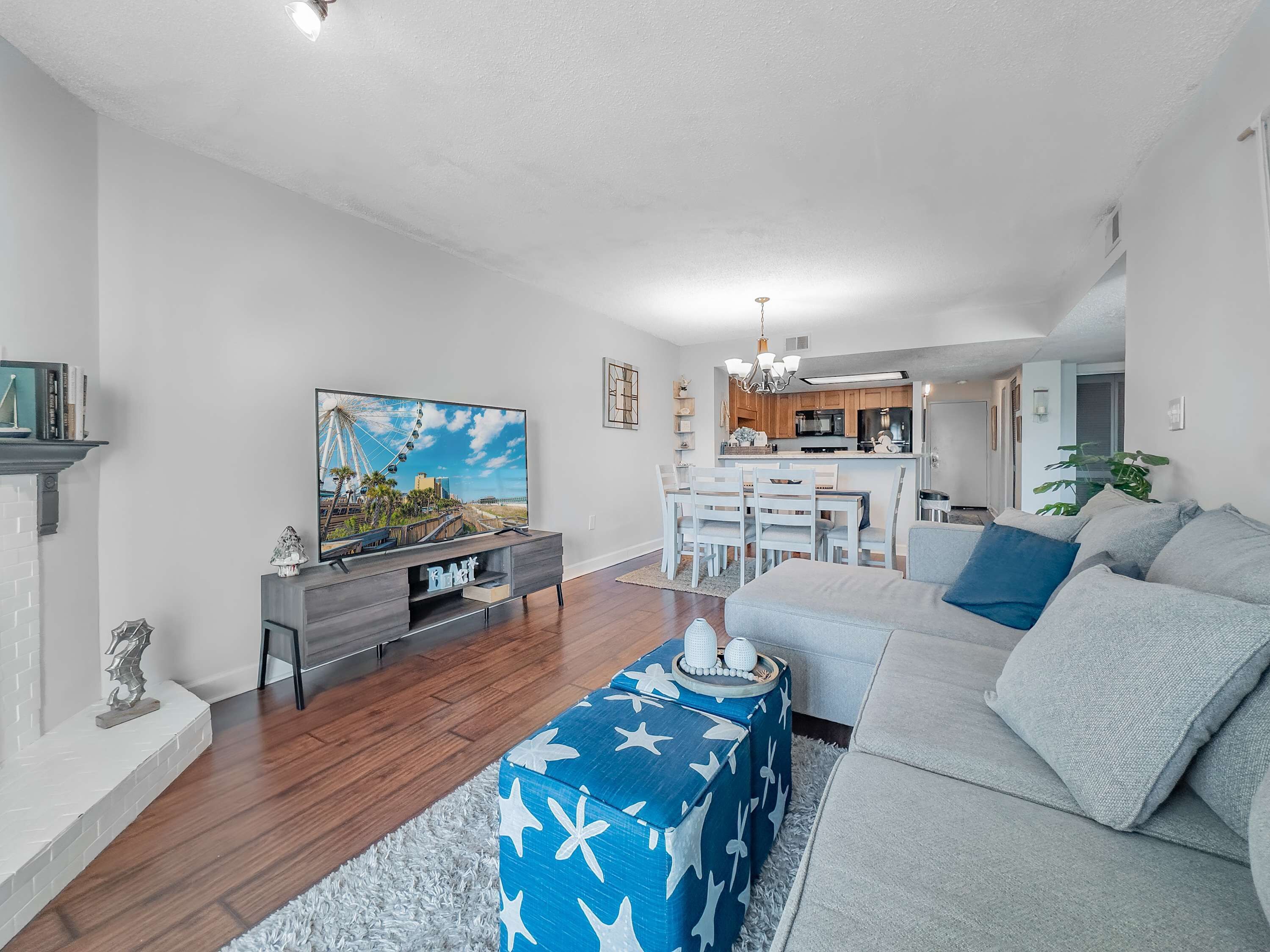 A modern living room with a flat-screen TV, a sofa, and a dining area with a kitchen in the background.