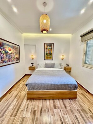 A bedroom with a large bed, wooden flooring, a hanging light fixture, and two wall-mounted lamps. - The Helio Estate Suite (Almazah)