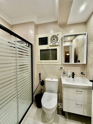 A bathroom with a toilet, sink, mirror, and window. - The Helio Estate Suite (Almazah)