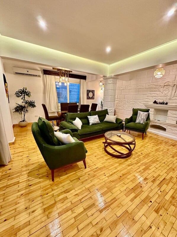 A living room with a green sofa set, a round coffee table, and a fireplace. - The Helio Estate Suite (Almazah)