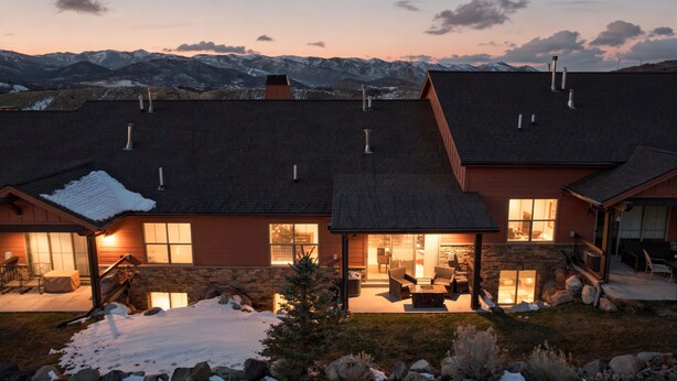 Une maison avec une façade en pierre, un patio couvert et une vue sur des montagnes enneigées.