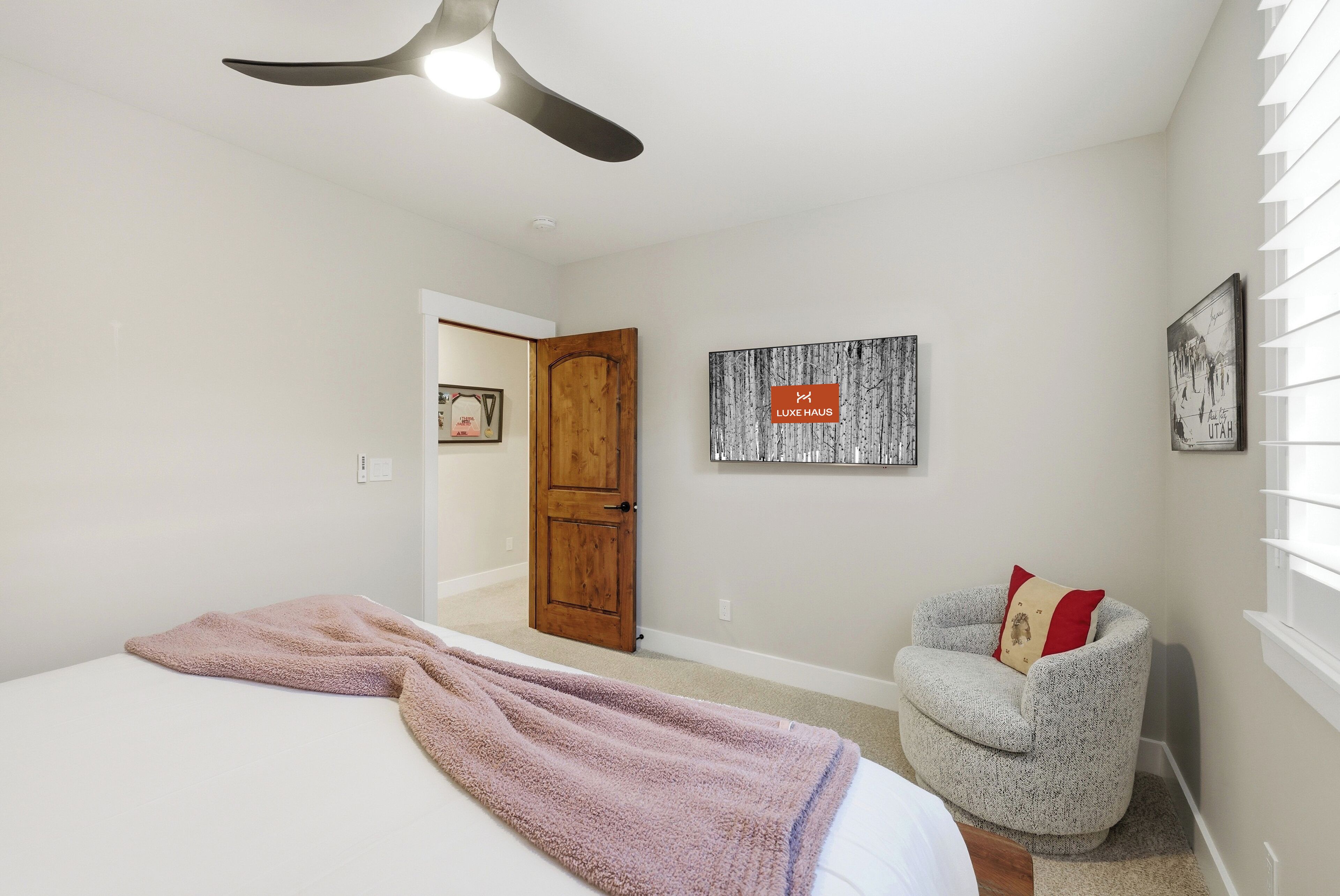 Une chambre à coucher avec un lit, un ventilateur de plafond, une chaise et des œuvres d’art accrochées aux murs.