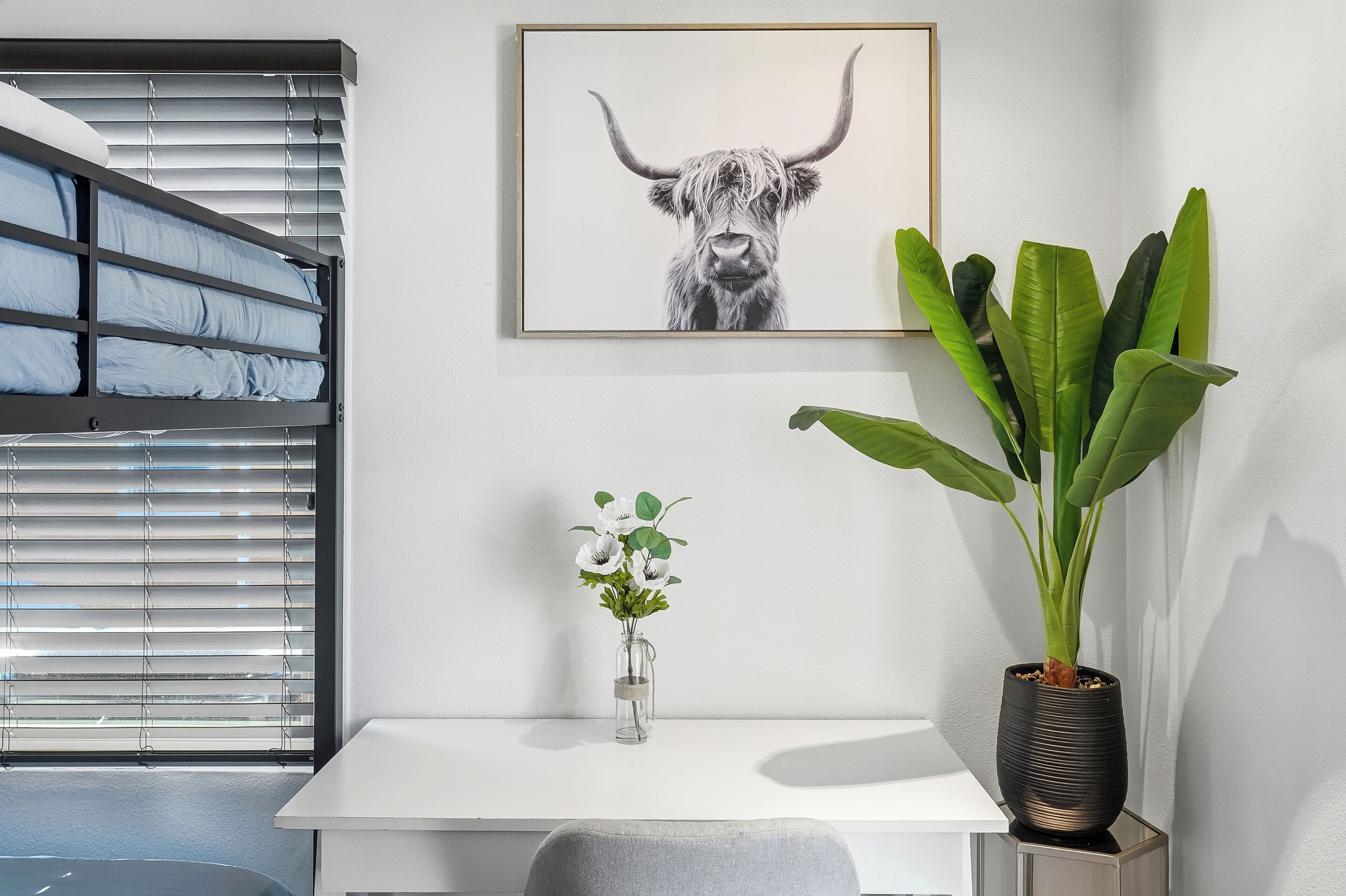 Una habitación moderna con una litera, una obra de arte enmarcada de un toro, una planta en maceta y un florero con flores.