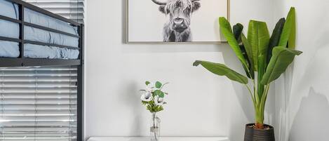 Una habitación moderna con una litera, una obra de arte enmarcada de un toro, una planta en maceta y un florero con flores.
