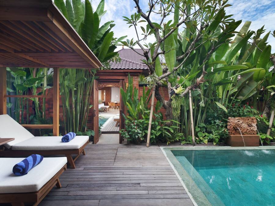 A wooden deck with lounge chairs, a pool, and lush tropical plants.