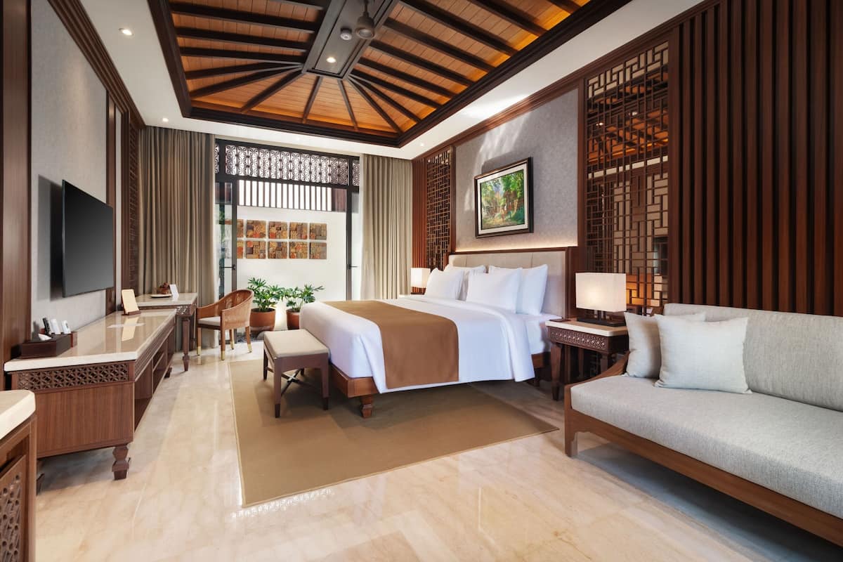 A hotel room with a bed, a sofa, a desk, a TV, and a window with curtains.