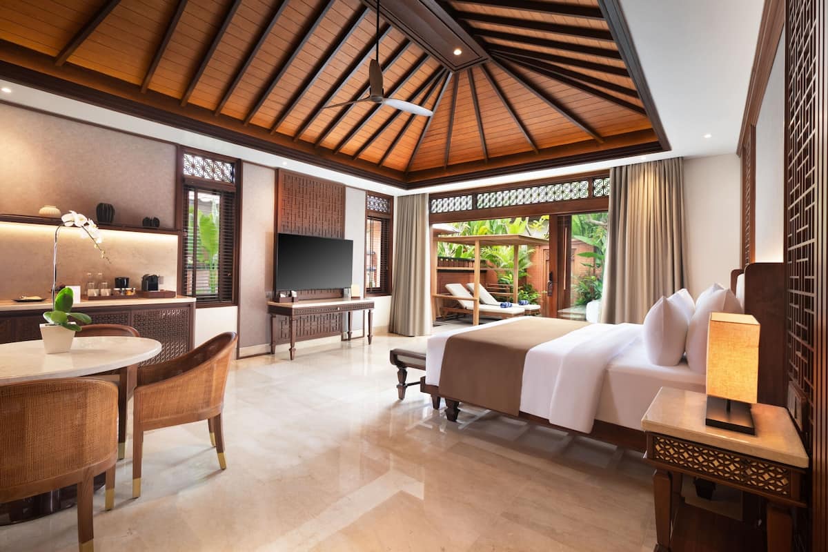 A hotel room with a bed, a desk, a TV, a dining area, and a view of the outdoors.