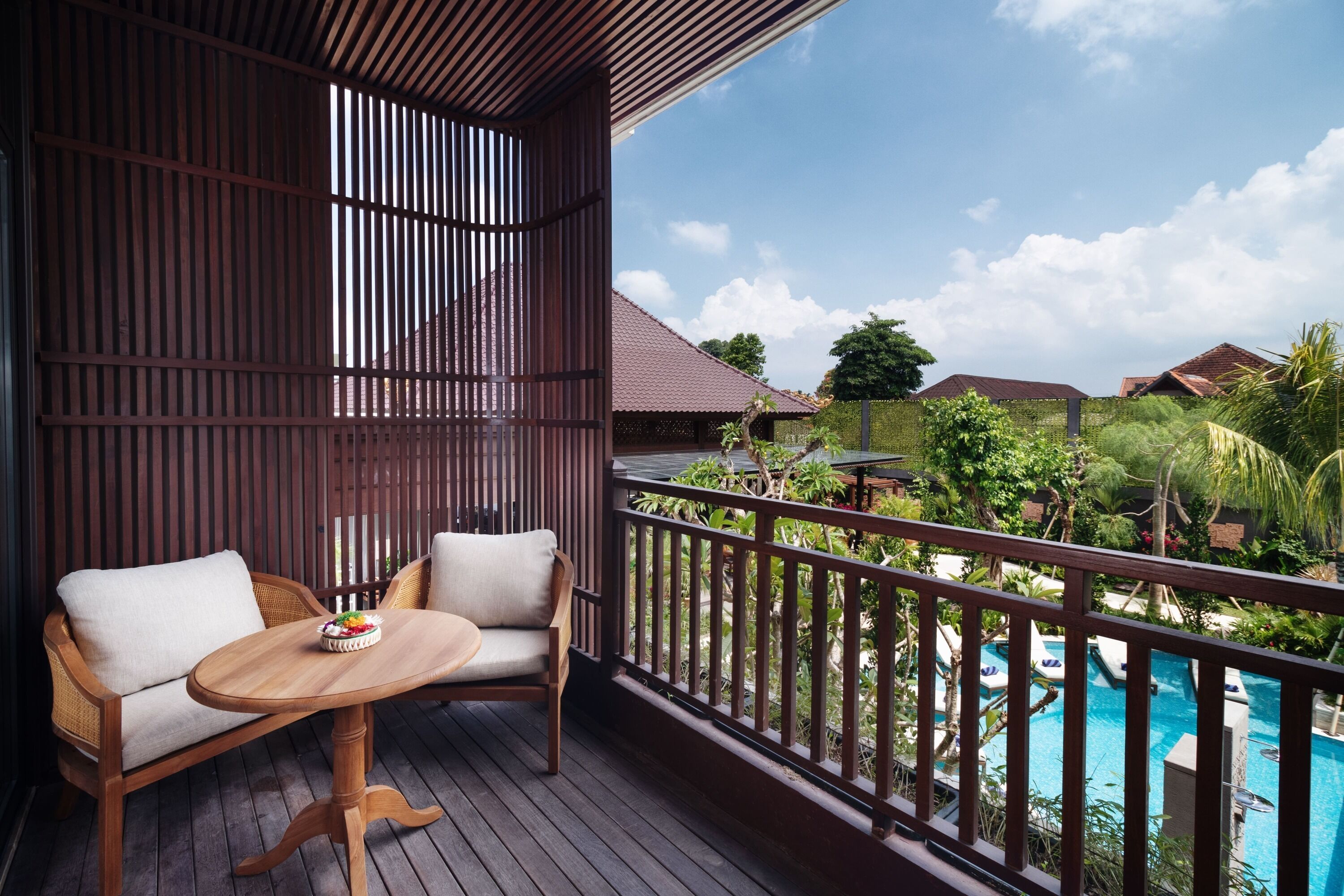 Une terrasse en bois avec une table et deux chaises, donnant sur une piscine et une végétation luxuriante.