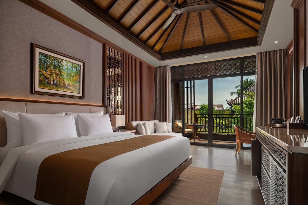 A spacious bedroom with a large bed, a desk, and a balcony with a view.