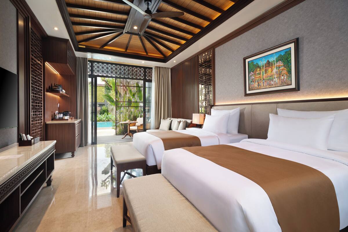 A hotel room with two beds, a desk, a TV, and a view of the outdoors.