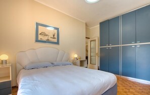 Ein Schlafzimmer mit Bett, Nachttischlampen, einem Kleiderschrank und einem gerahmten Bild an der Wand.
