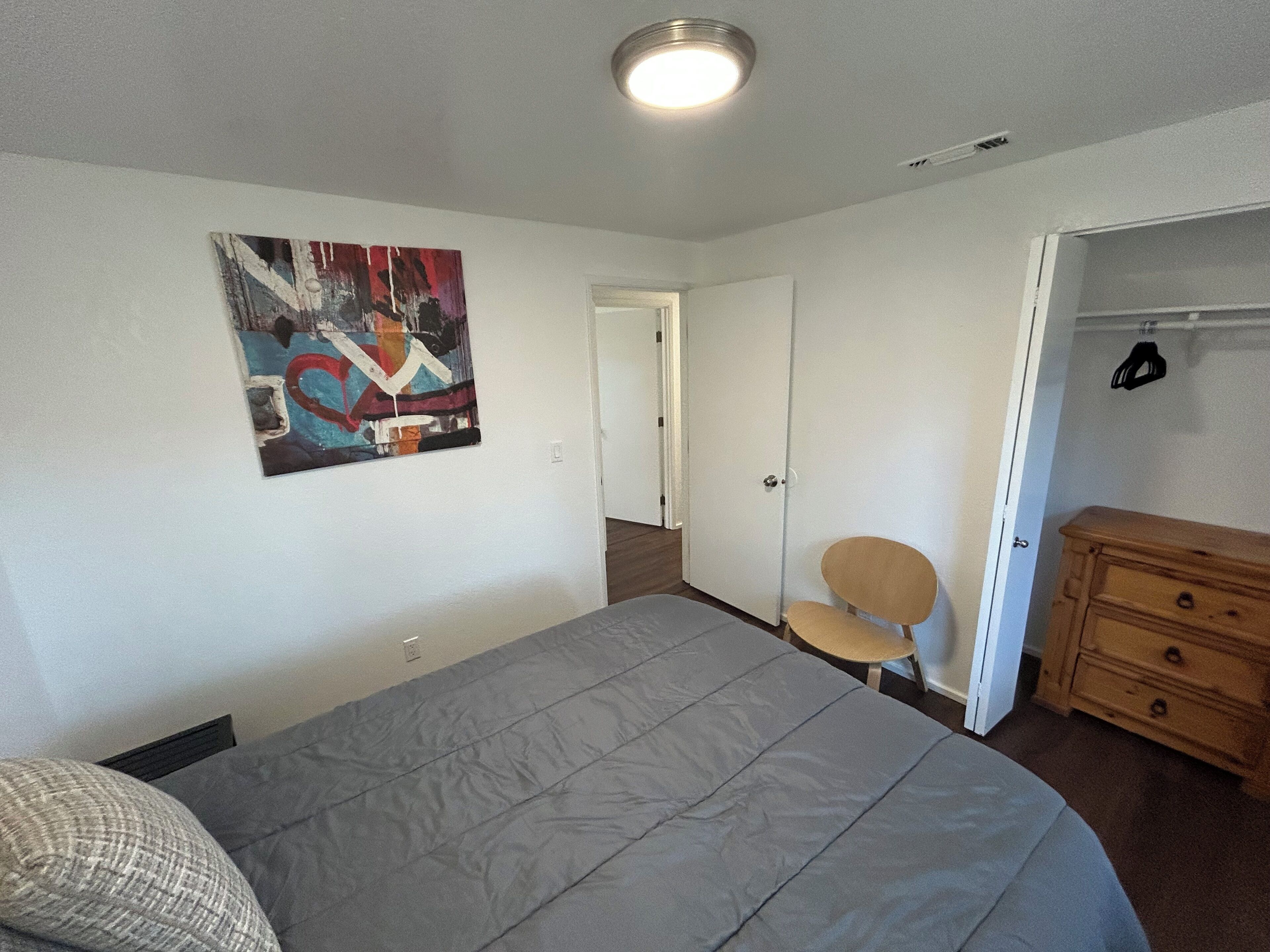 Une chambre à coucher comprenant un lit, une chaise, une commode et une porte donnant sur une autre pièce.