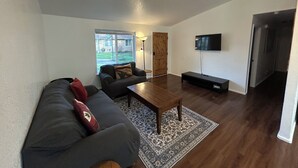 Ein Wohnzimmer mit einer Couch, einem Couchtisch, einem Fernseher und einer Tür zu einem weiteren Raum.