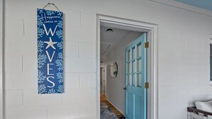 Un pasillo con una puerta azul, una pared blanca con un letrero que dice 'WIVES' y dos taburetes blancos.