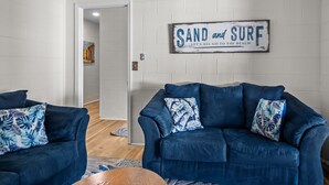 Una sala de estar con un sofá azul, una mesa de centro de madera y un letrero en la pared que dice "SAND and SURF".
