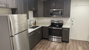 Una cocina moderna con armarios oscuros, electrodomésticos de acero inoxidable y suelo de madera.