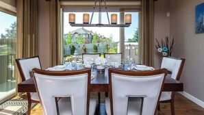 Une salle à manger avec une grande table dressée pour six personnes, des chaises blanches et un lustre.