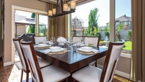 Une salle à manger avec une table en bois foncé, dressée pour six personnes, des chaises à revêtement blanc et un lustre à plusieurs lampes.