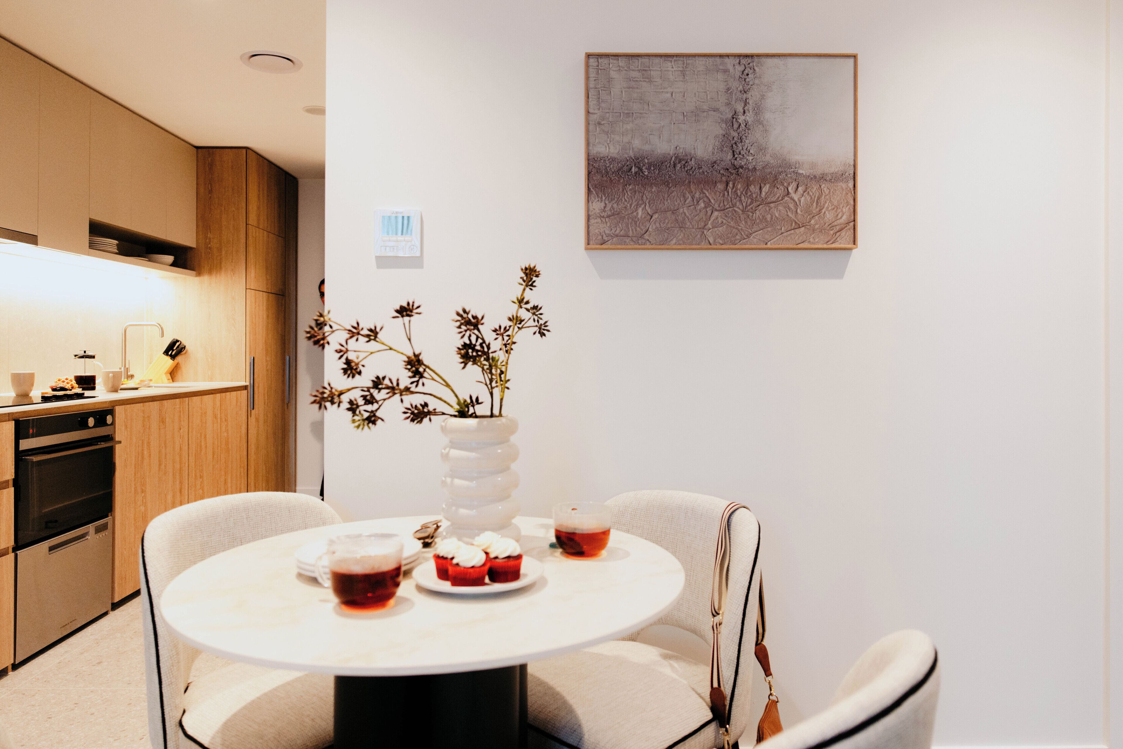 Una cocina moderna con armarios de madera, una mesa de comedor con sillas y un florero con flores secas.