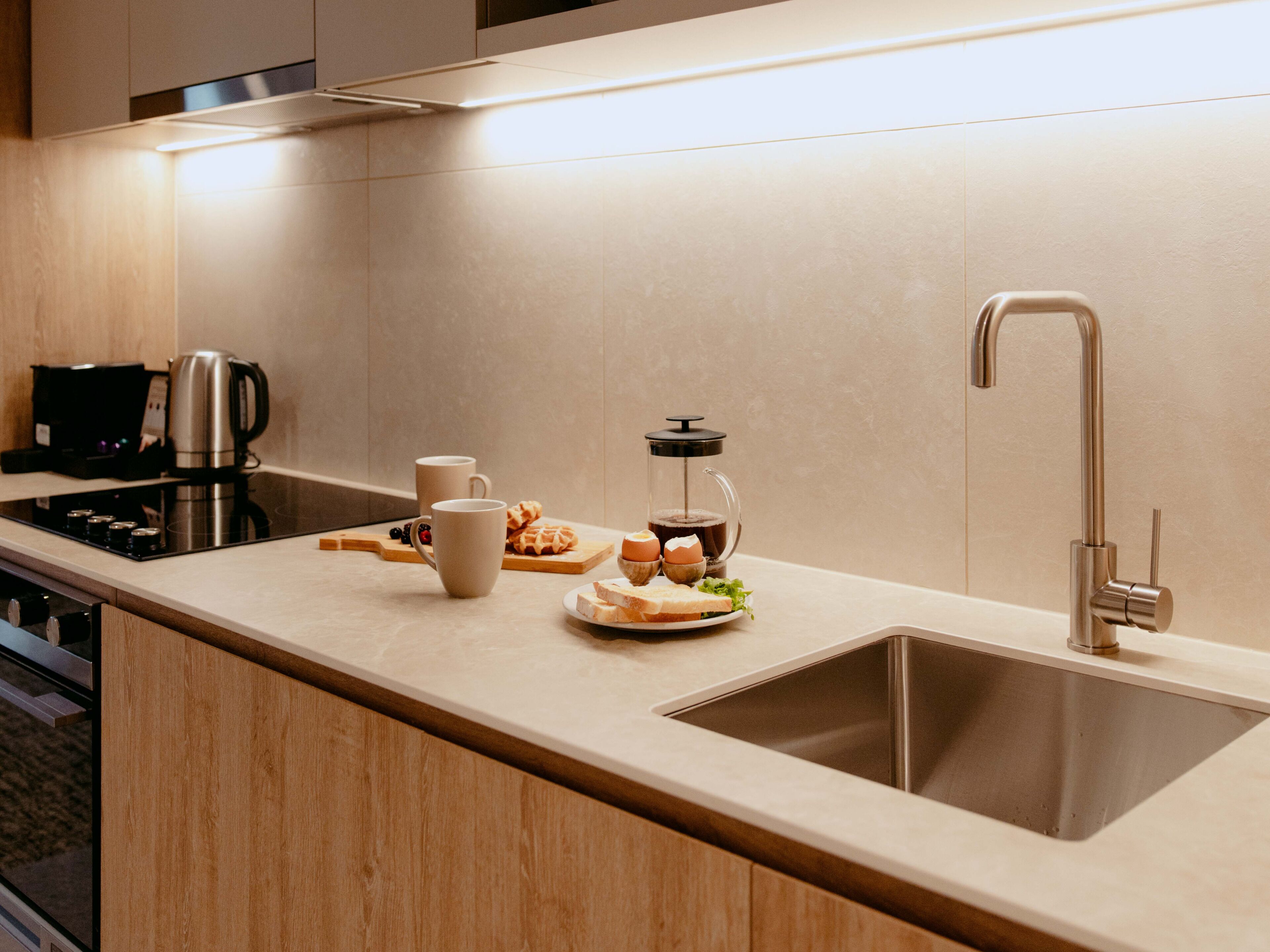 A modern kitchen with a stainless steel sink, a coffee maker, and a glass carafe on the counter.