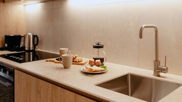 Una cocina moderna con un lavamanos de acero inoxidable, una cafetera y una jarra de vidrio sobre la encimera.